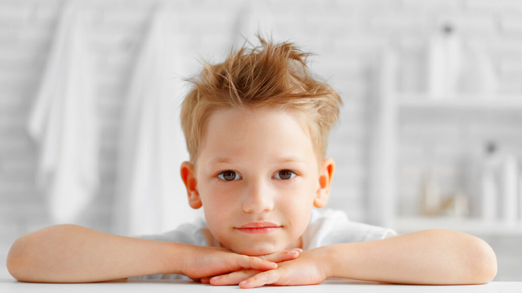 Stylish young boy with sandy blonde hair wearing a structured and modern precision boys haircut.