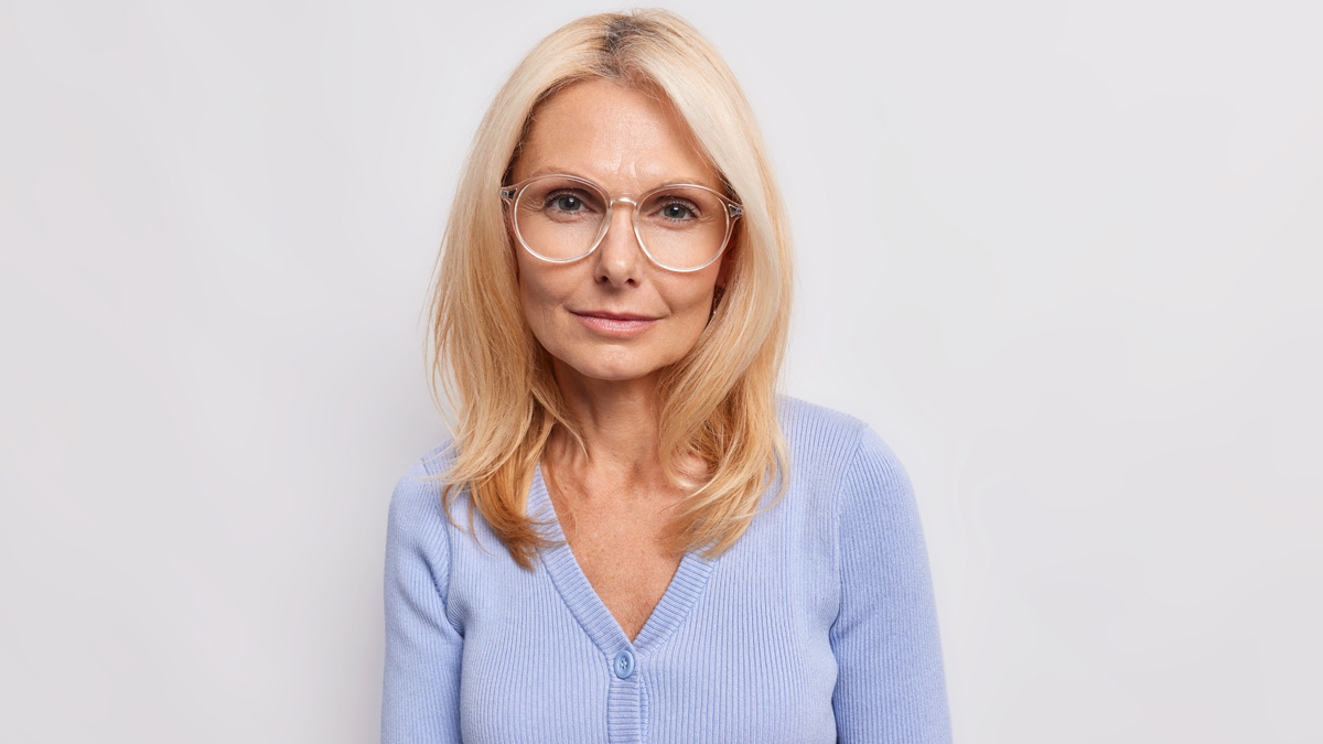 A waist-up shot of a serenely smiling mature woman with a butterfly frame haircut against a neutral background.