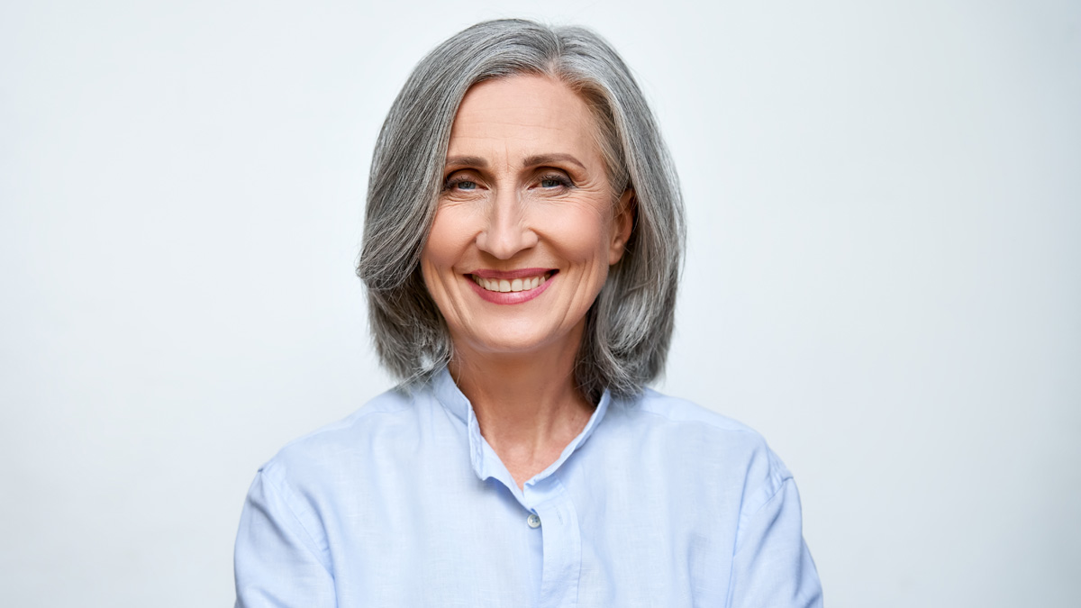 A smiling woman with a short, straight gray c-curve midi haircut wearing a light blue collared shirt.