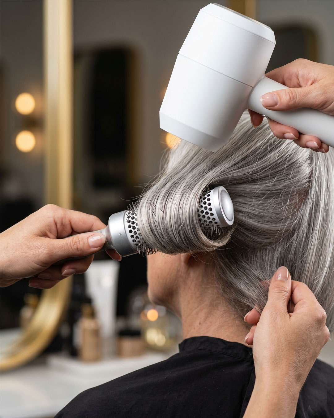 Stylist using a round brush to blow-dry silver hair inward.