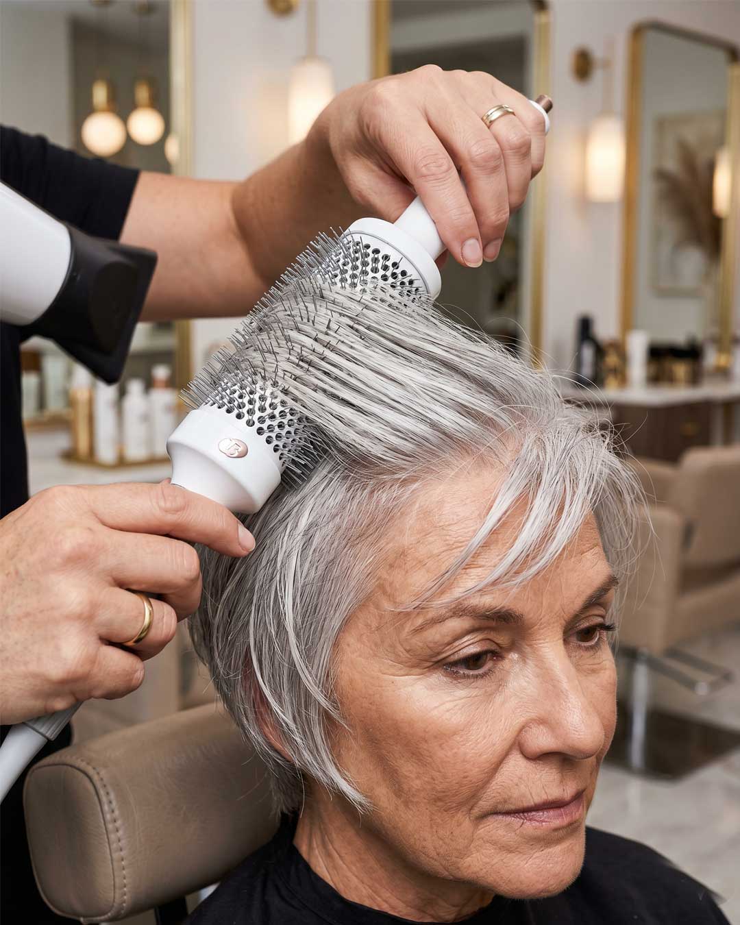 Stylist using a round brush to over-direct silver face-framing layers.