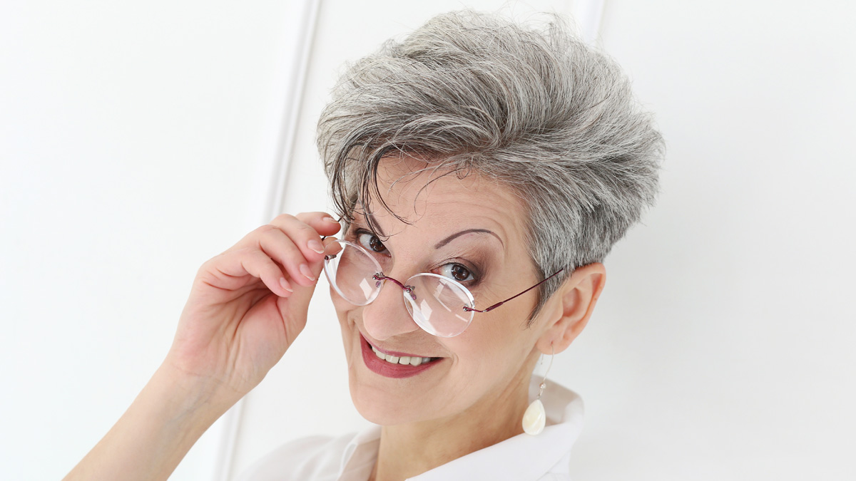 A beautiful woman looking directly at the camera, smiling with a short, silver-halo crop haircut.